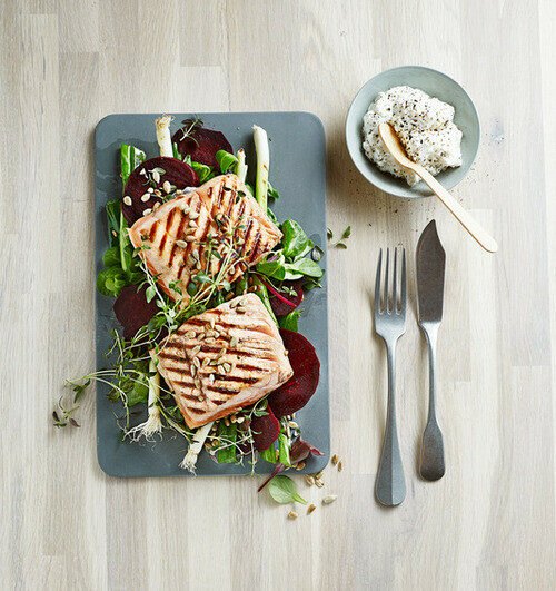 Grilled salmon fillets served on a bed of fresh greens, sliced beets, and spring onions with a side of herb-infused cream.